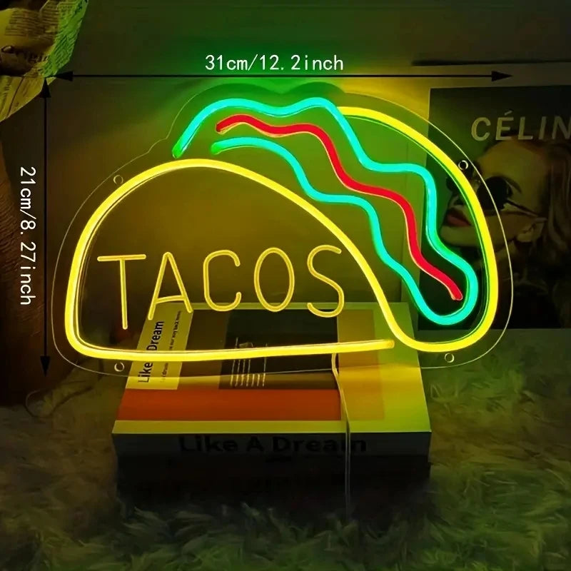 Neon sign shaped like a taco with 'TACOS' text, placed on a surface with a blurred background.