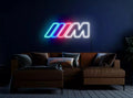 Neon sign with a logo on a dark wall above a brown sofa.