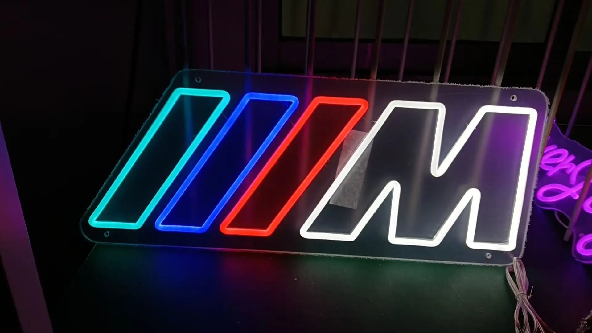 Neon sign with colorful BMW M logo on a dark background