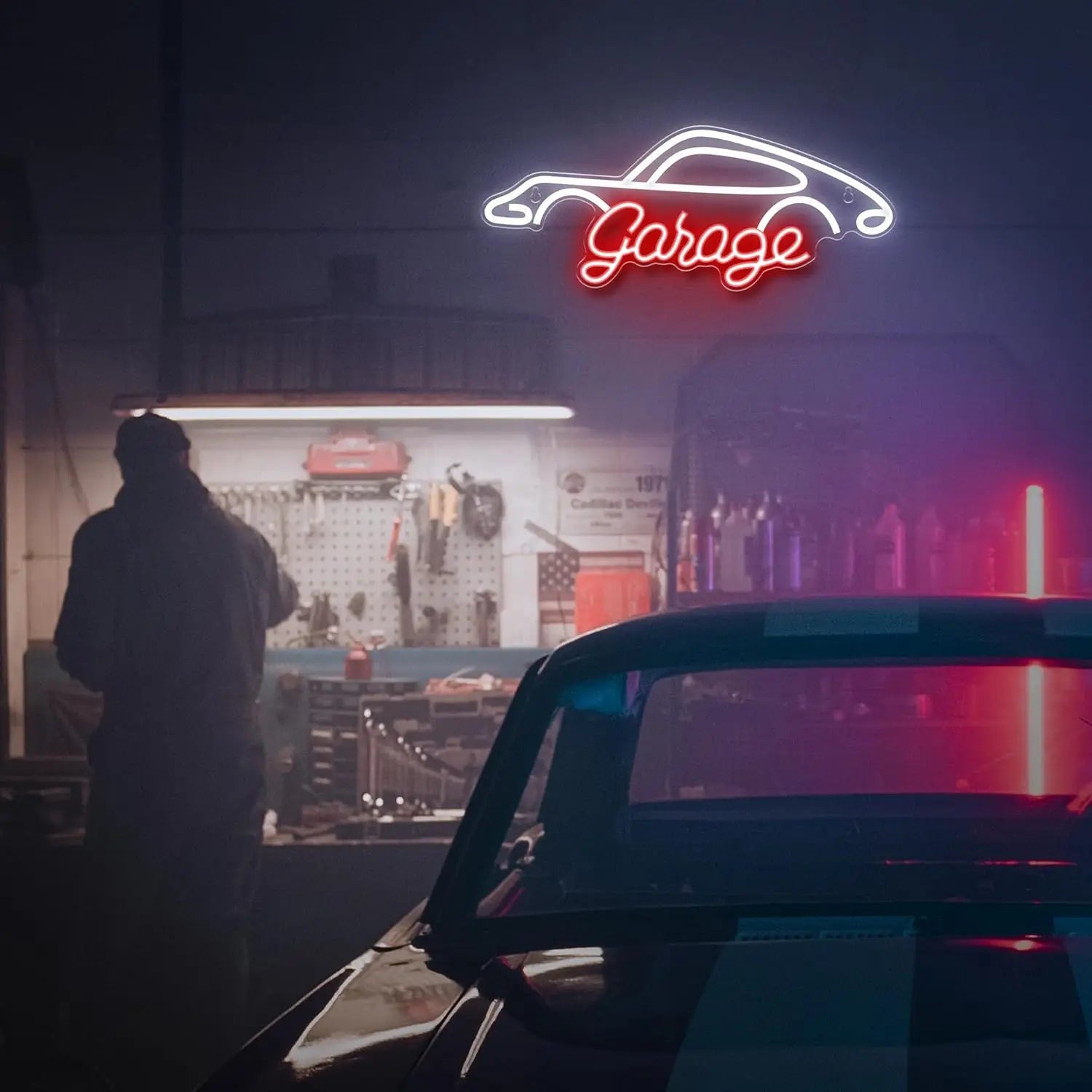 Neon 'Garage' sign above a car workshop with a person standing inside.