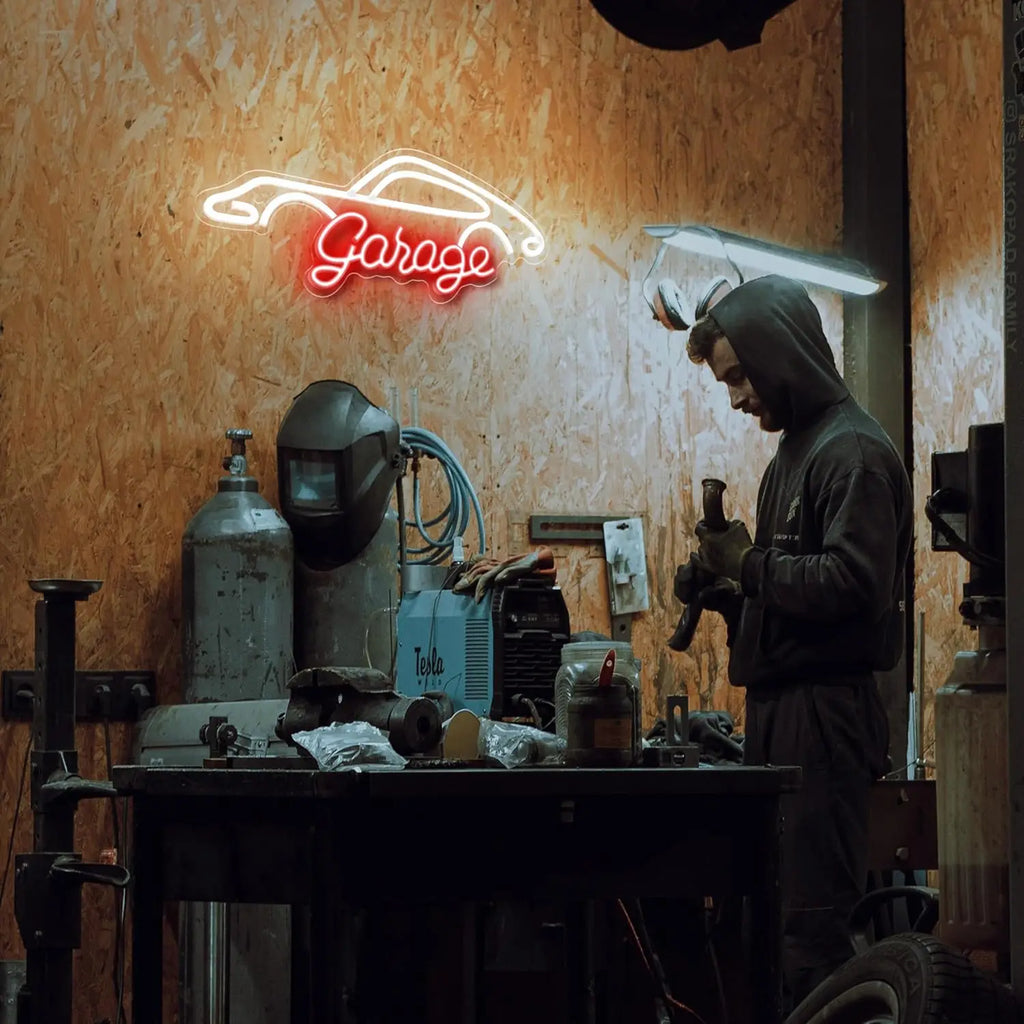 Person working in a garage with a neon 'Garage' sign on the wall.
