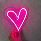 Neon pink heart-shaped light held by a hand against a dark background