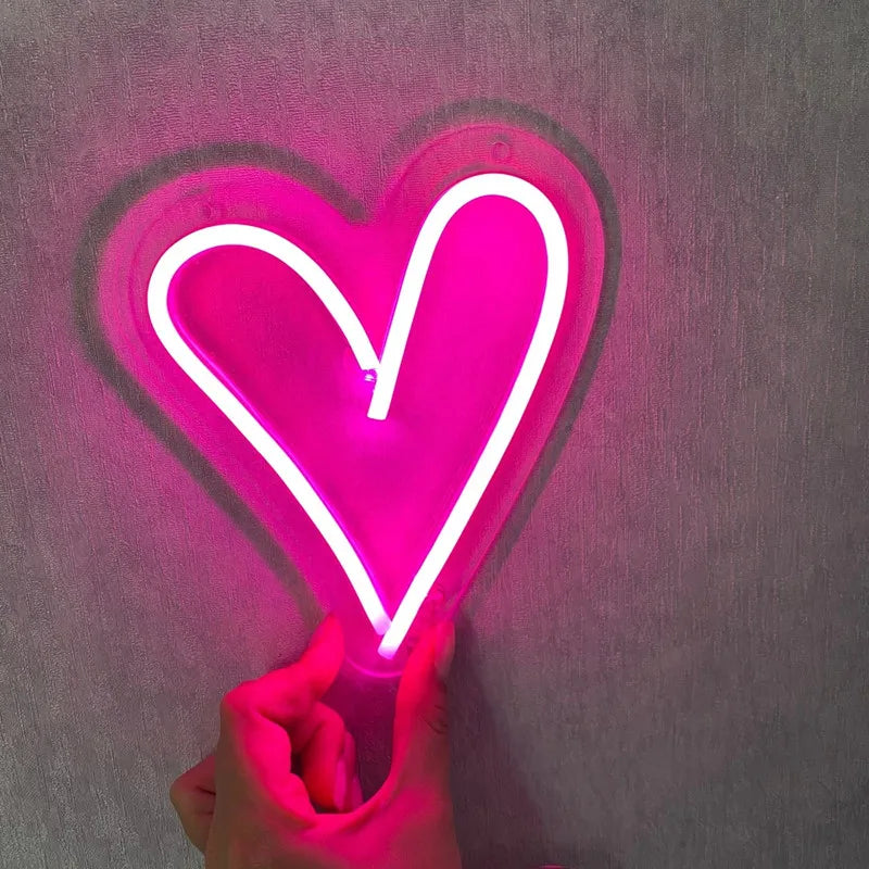 Neon pink heart-shaped light held by a hand against a dark background